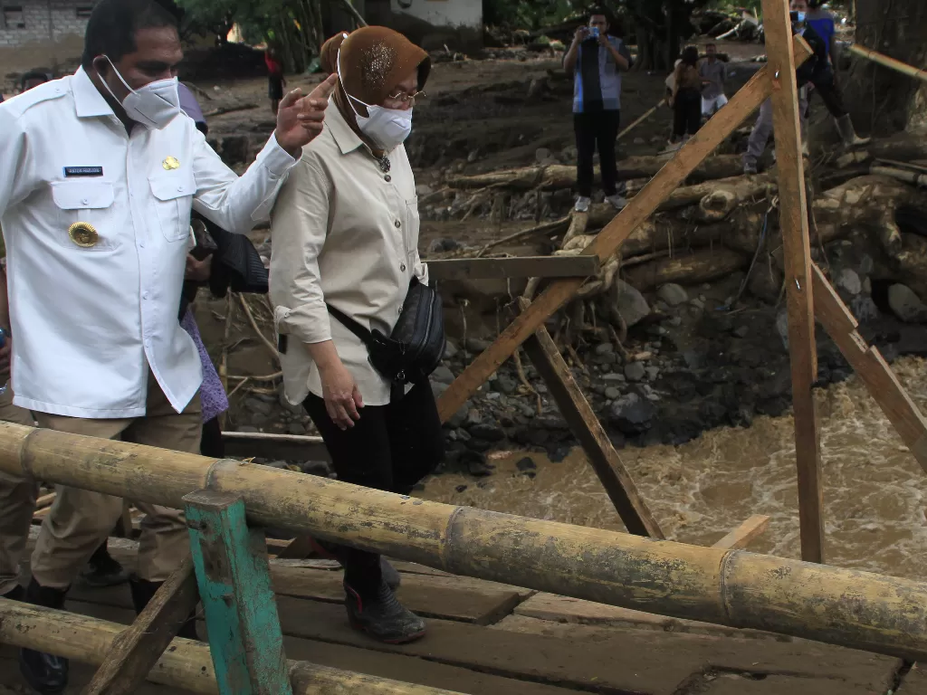 Menteri Sosial Tri Rismaharini (kanan) didampingi Bupati Flores Timur Anthon Hadjon berjalan melewati jembatan darurat saat meninjau lokasi banjir bandang di Desa Waiburak, Kecamatan Adonara Timur, NTT, Selasa (6/4/2021). (ANTARA FOTO/Kornelis Kaha)