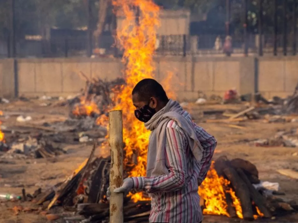  Seorang pria berjalan melewati pembakaran tumpukan kayu pemakaman orang, yang meninggal karena penyakit virus corona (COVID-19), di tempat krematorium di New Delhi, India, Kamis (22/4/2021). (REUTERS/DANISH SIDDIQUI) 