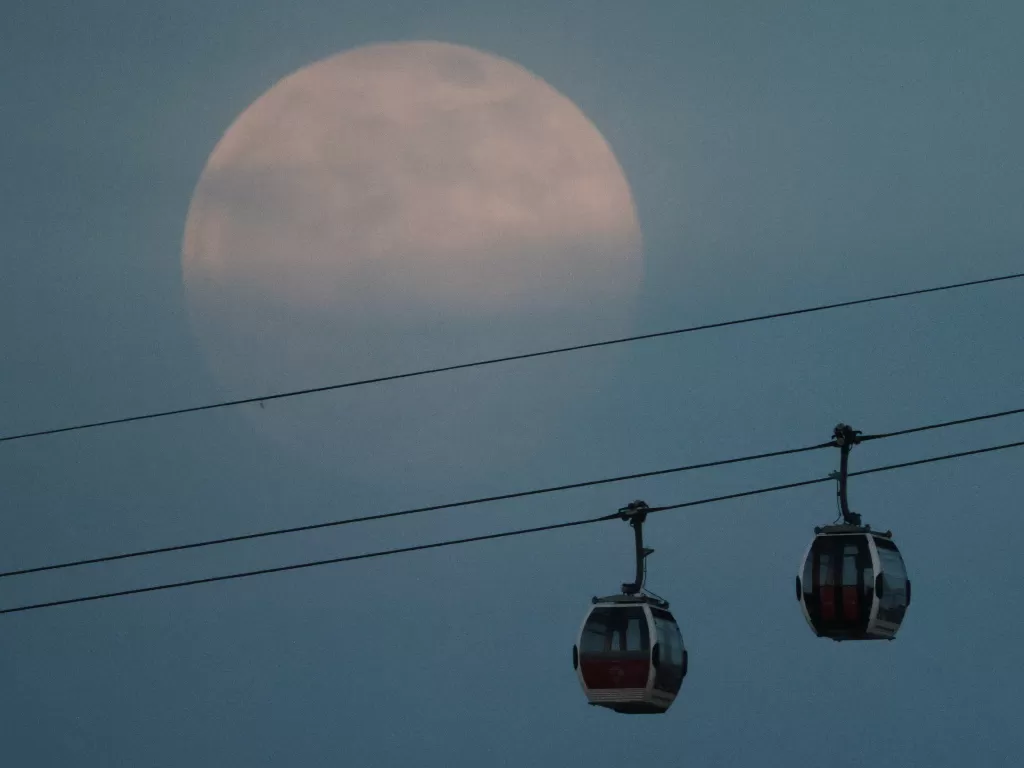Bulan purnama, juga dikenal sebagai Supermoon, muncul di atas kereta gantung Emirates Air Line di London, Inggris, 26 April 2021 waktu setempat. (photo/REUTERS/Hannah McKay)