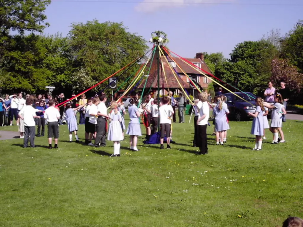 Anak-anak menari di sekitar tiang besar sebagai bagian dari perayaan May Day di Welwyn, Inggris. (Wikipedia).
