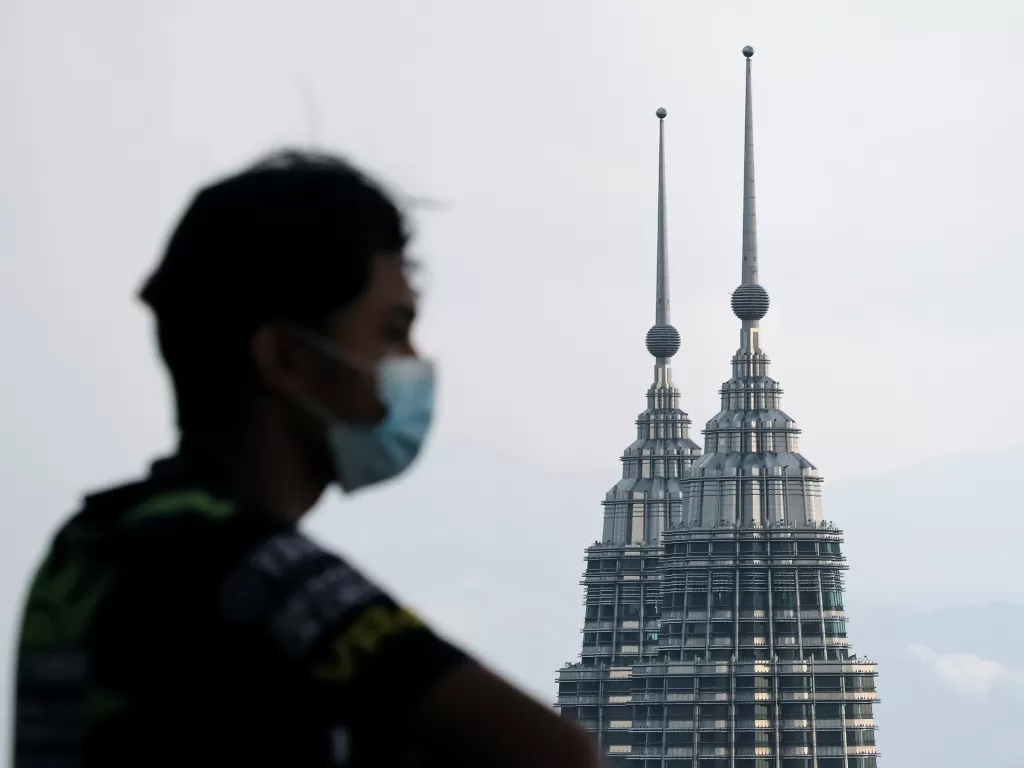 Seorang warga Malaysia menggunakan masker untuk pencegahan Covid-19 berlatar belakan Twin Tower Petronas, Kuala Lumpu. (REUTERS/Lim Huey Teng).