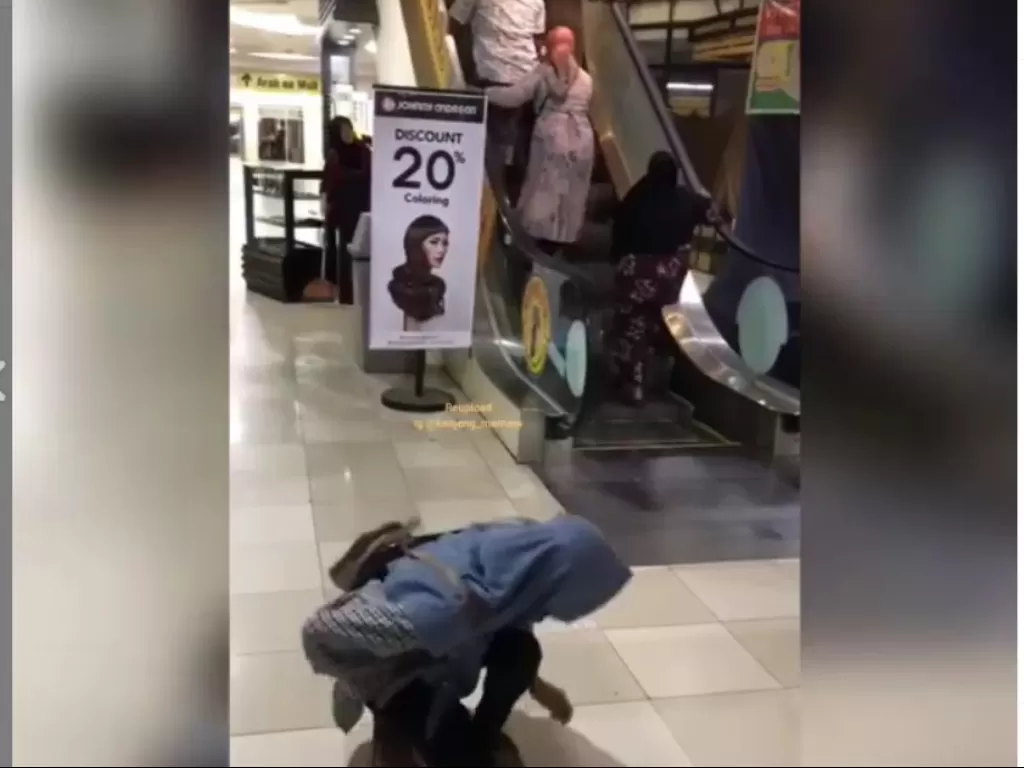 Seorang perempuan terlihat tertawa melihat ibu-ibu salah naik eskalator (screenshot video)