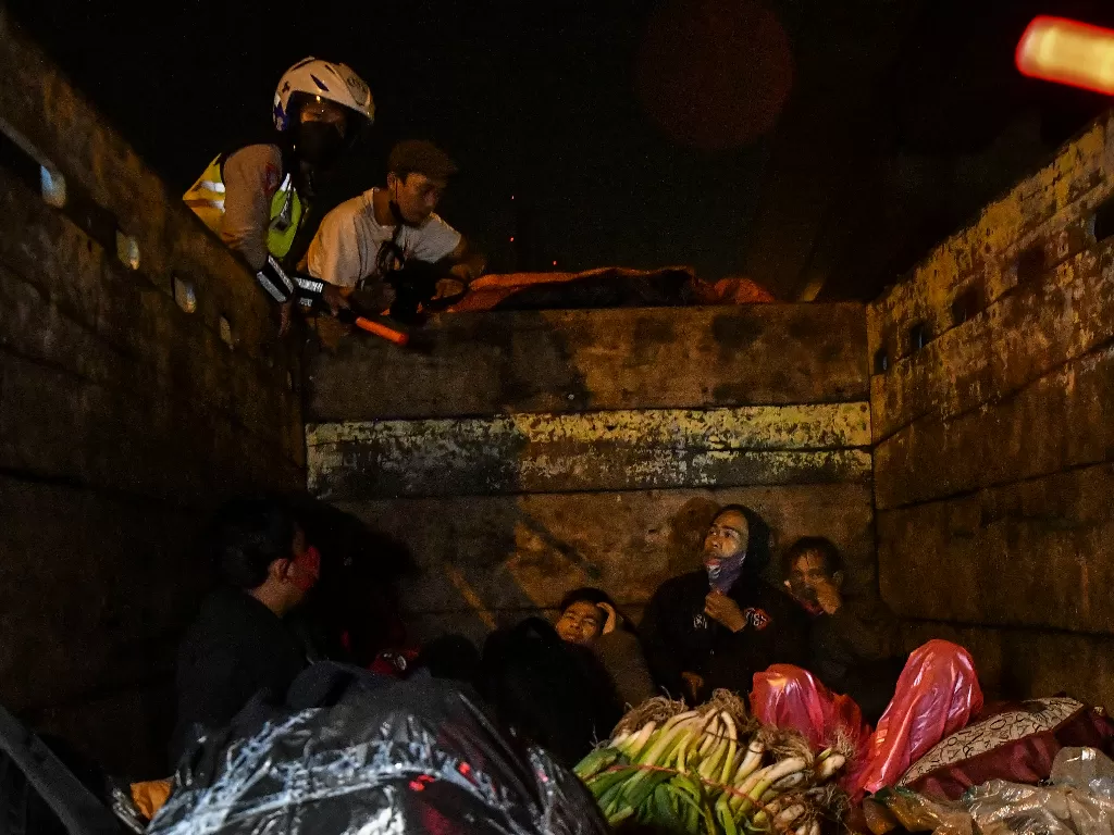 Petugas Kepolisan (kiri) memeriksa truk bermuatan sayur yang membawa pemudik saat melintas di check point penyekatan arus mudik di Tol Cikarang Barat, Kabupaten Bekasi, Jawa Barat, Kamis (6/5/2021) dini hari. (Antara)