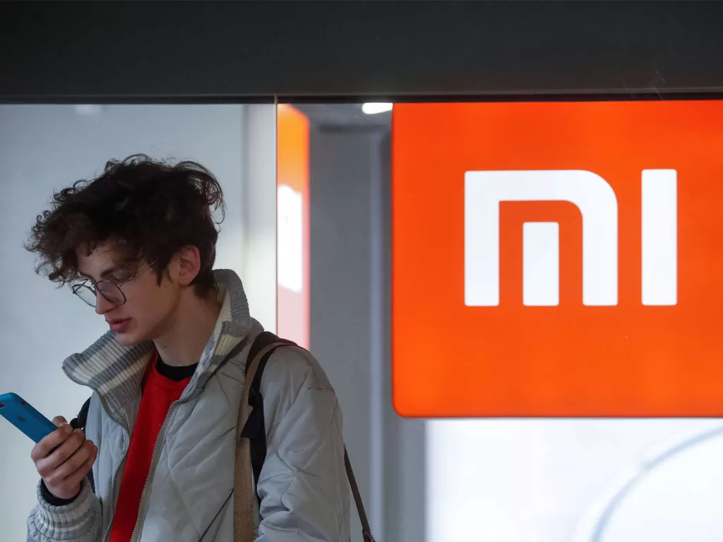 Seorang pria sedang menggunakan smartphone di depan logo Xiaomi (photo/REUTERS/Valentyn Ogirenko)