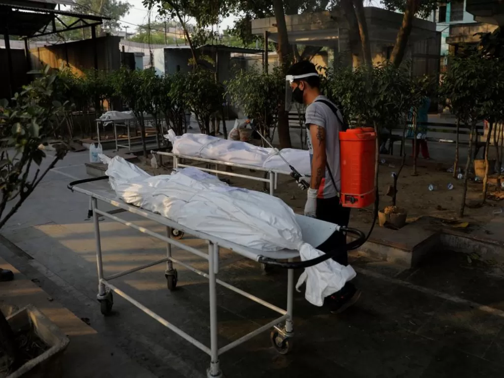 Petugas menyemprotkan cairan disinfektan ke kantong jenazah pasien Covid-19 di India. (REUTERS/Adnan Abidi)