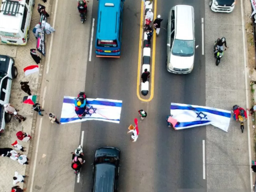 Lembaga Kemanusiaan, Asar Humanity menggelar aksi bela Palestina dengan cara mengibarkan bendera Palestina dan menaruh dua bendera Israel berukuran raksasa di tengah jalan raya Parung, Kabupaten Bogor, Jawa Barat. (Dok. Roozika Sunandila)