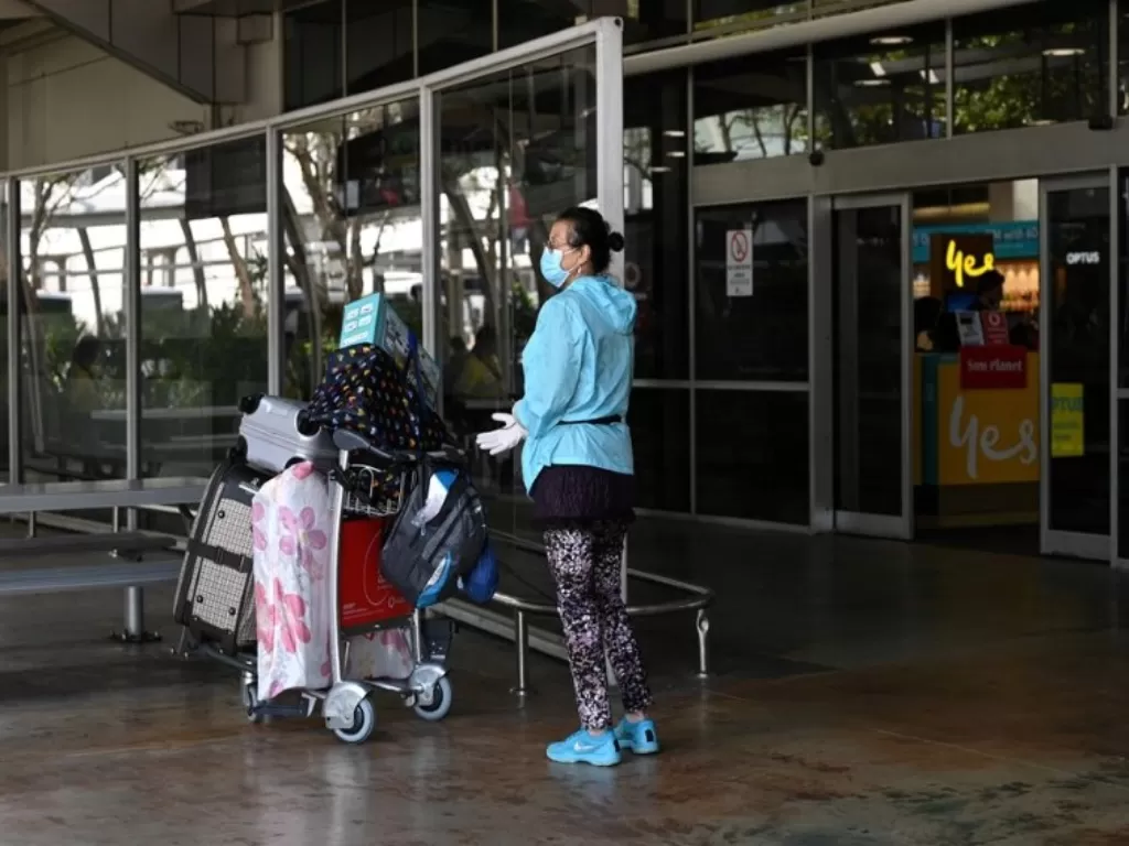 Seorang pelancong yang mengenakan masker pelindung wajah dan sarung tangan berangkat dari bagian kedatangan di terminal internasional Bandara Internasional Kingsford Smith pada pagi hari setelah Australia menerapkan larangan masuk bagi non-warga negara da