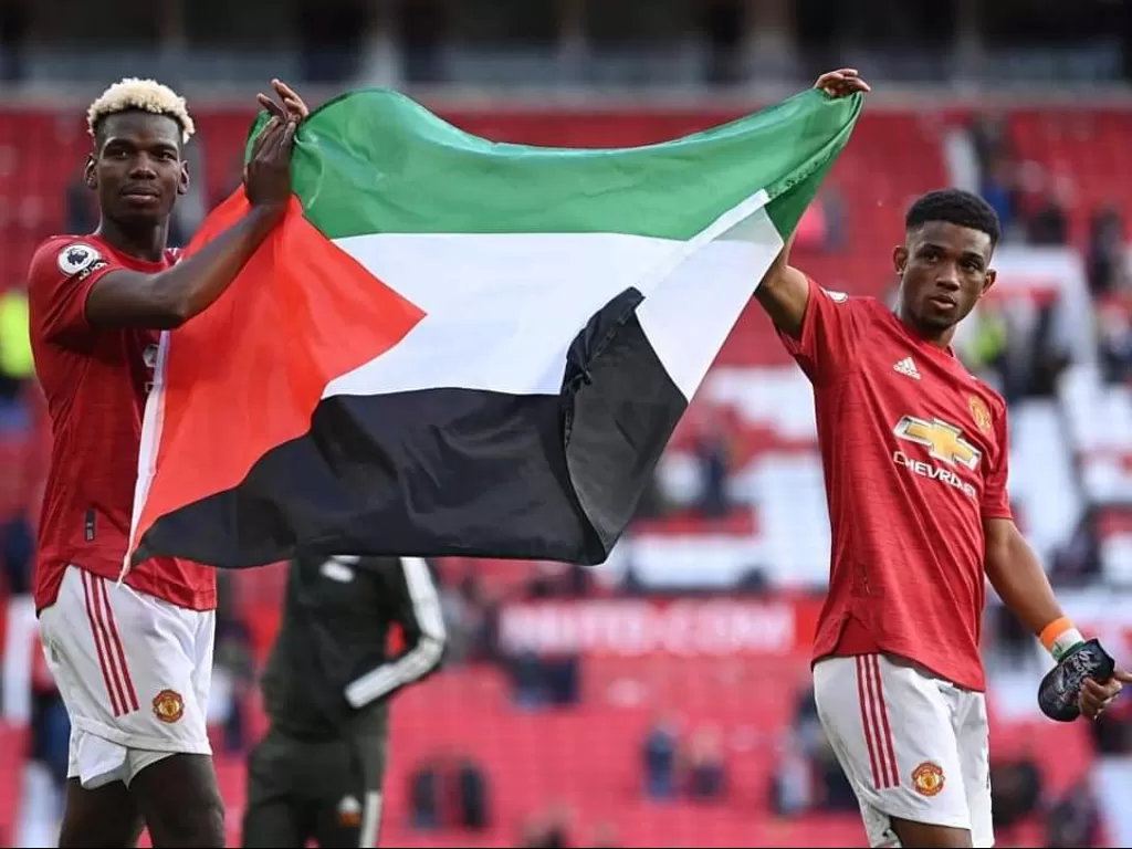 Paul Pogba dan Amad Dialo membentangkan bendera Palestina usai laga melawan Fulham di Old Trafford, Rabu (19/5/2021). (Twitter/@ManUtdMEN)