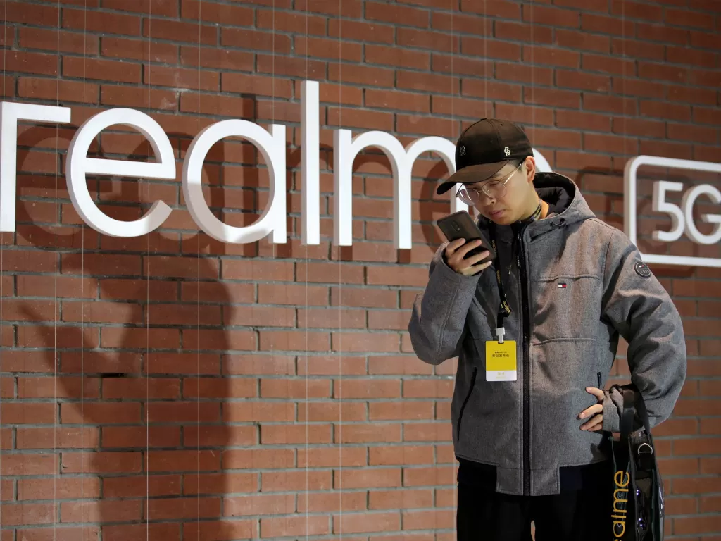 Tampilan seorang pria berada di depan logo perusahaan Realme (photo/REUTERS/Jason Lee)