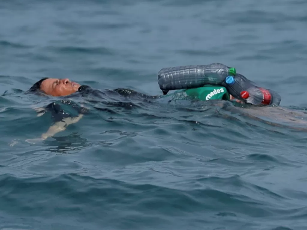 Seorang bocah menyebrangi laut menggunakan botol plastik. (Photo/Reuters)
