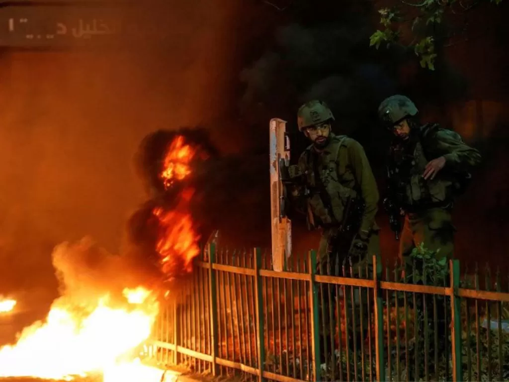 Tentara Israel berdiri di samping pembakaran ban saat warga Palestina mengambil bagian dalam protes anti-Israel atas ketegangan di Yerusalem, di Hebron di Tepi Barat yang diduduki Israel, Senin (26/4/2021). (ANTARA FOTO/REUTERS).