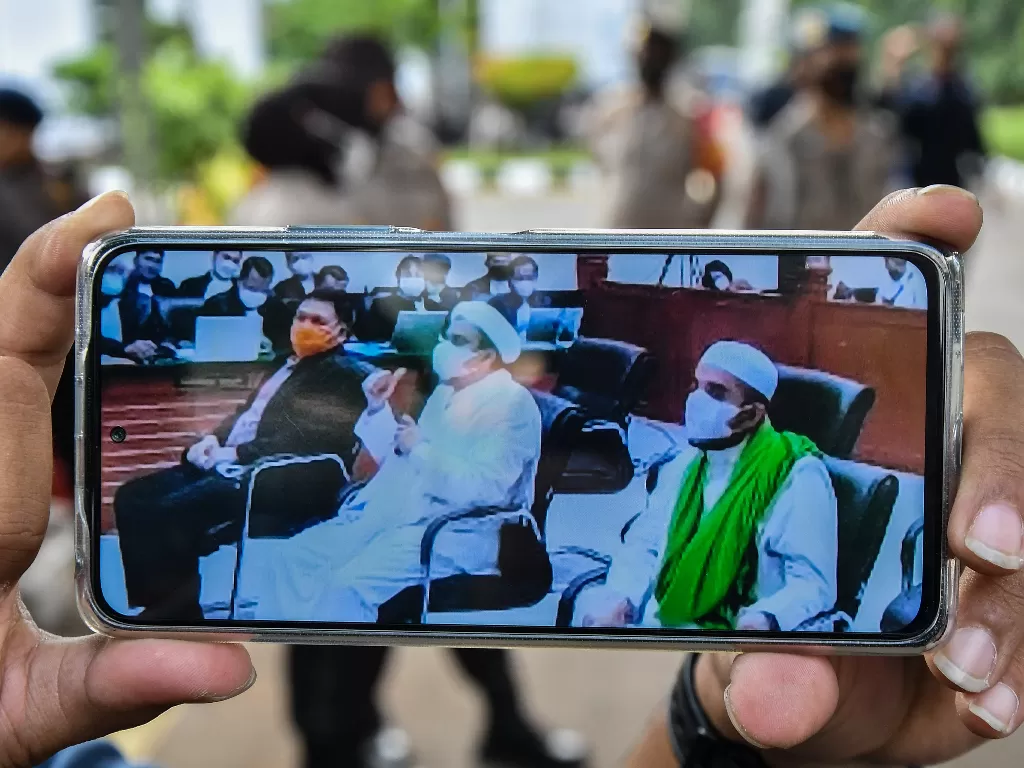 Layar telepon pintar menampilkan suasana sidang yang dihadiri Habib Rizieq Shihab (tengah), Direktur rumah sakit UMMI Andi Tatat (kiri) dan Habib Hanif Alatas (kanan) di Pengadilan Negeri Jakarta Timur, Kamis (27/5/2021). (ANTARA/Fakhri Hermansyah)