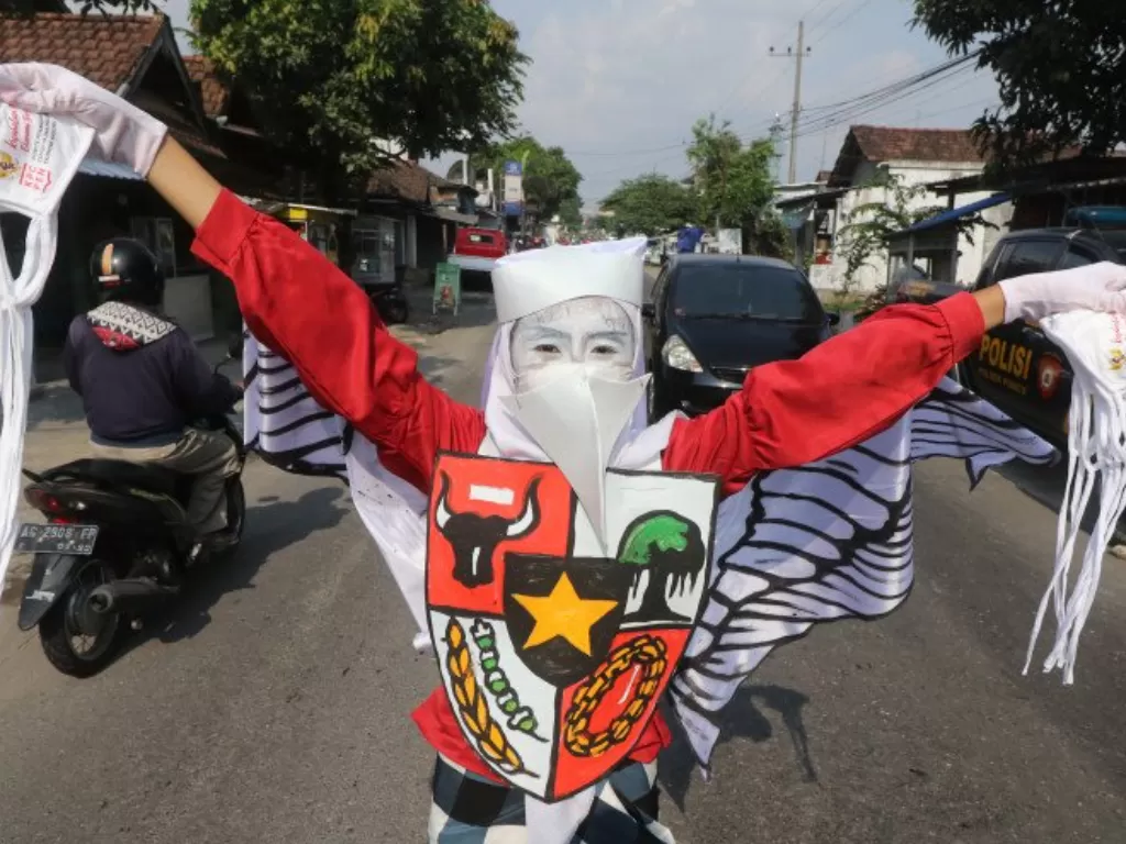 Seorang pelajar SMA Negeri 1 Puncu membagikan masker dengan mengenakan kostum unik bertema Garuda Pancasila di Kediri, Jawa Timur, Senin (31/5/2021). (ANTARA FOTO/Prasetia Fauzani)
