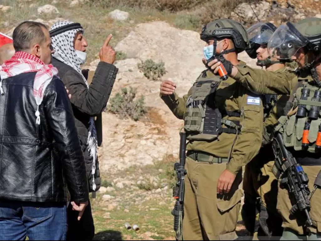 Seorang demonstran Palestina berdebat dengan tentara Israel selama protes terhadap pemukiman Israel, di Beit Dajan di Tepi Barat yang diduduki Israel, Jumat (8/1/2021). (REUTERS/Raneen Sawafta).