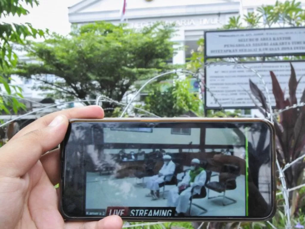 Jurnalis mengamati layar telepon pintar sidang Rizieq Shihab yang beragendakan tuntutan dari Jaksa Penuntut Umum (JPU) di Pengadilan Negeri Jakarta Timur. (ANTARA FOTO/Fakhri Hermansyah)