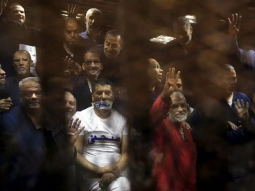 Anggota Ikhwanul Muslimin melambaikan empat jari melambangkan dukungan bagi anggota Ikhwanul Muslimin lain yang berada di pengadilan di pinggiran kota Kairo, Mesir. (REUTERS/Amr Abdallah Dalsh).