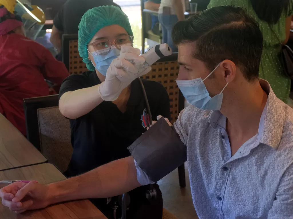 Petugas kesehatan memeriksa suhu tubuh Warga Negara Asing (WNA) yang menjalani vaksinasi dosis kedua (ANTARA FOTO/Nyoman Hendra Wibowo)