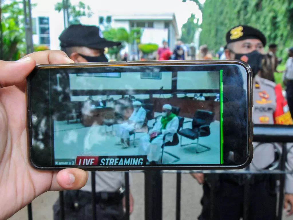 Jurnalis mengamati layar telefon pintar sidang Rizieq Shihab yang beragendakan tuntutan dari Jaksa Penuntut Umum (JPU) di Pengadilan Negeri Jakarta Timur. (Foto: ANTARA/Fakhri Hermansyah)