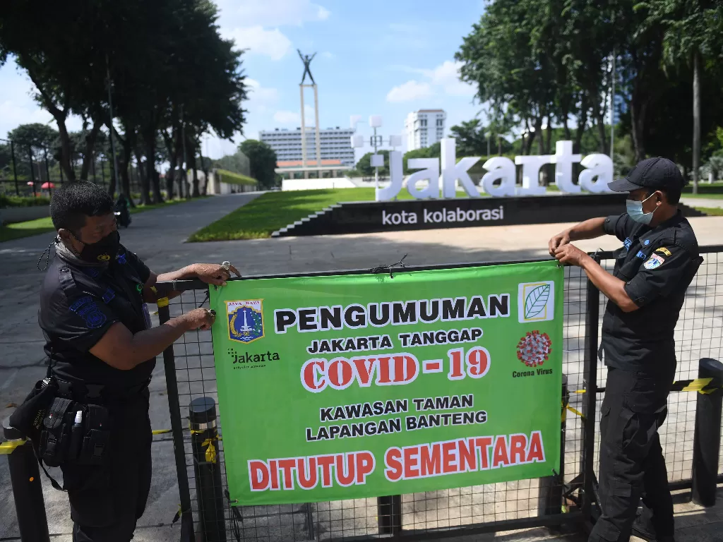 Petugas gabungan merapikan spanduk pengumuman ditutupnya Taman Lapangan Banteng di Jakarta, Jumat (25/6/2021). (ANTARA/Akbar Nugroho/Gumay)