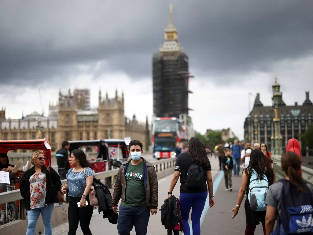 Orang-orang berjalan mengenakan masker di atas Jembatan Westminster, London. (REUTERS/Henry Nicholls)