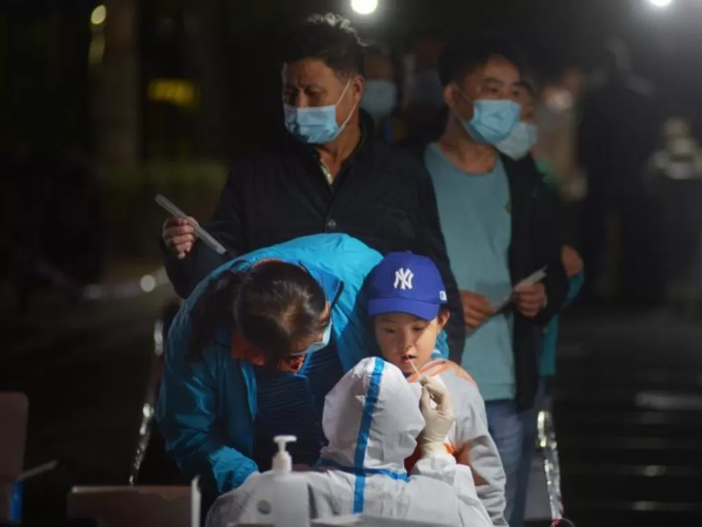 Petugas kesehatan dengan hazmat melakukan tes swab Covid-19 pada seorang anak laki-laki di Qingdao, Shandong, Tiongkok, Selasa (13/10/2020). (REUTER/Scnsphoto)