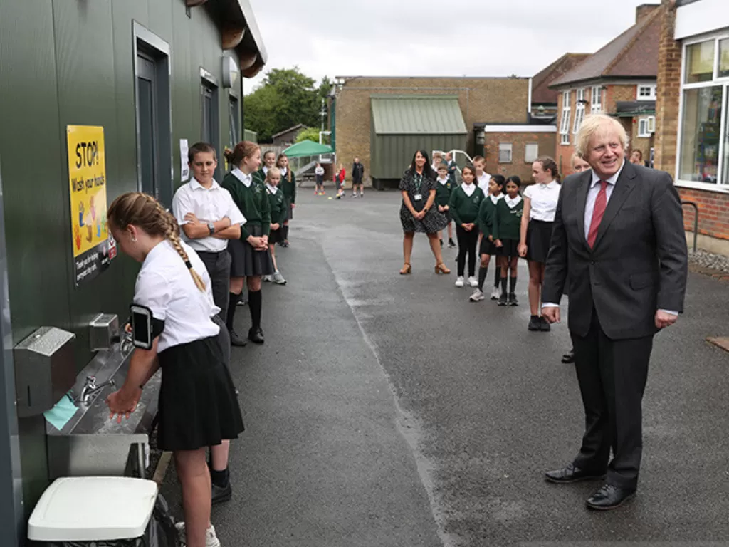 Perdana Menteri Inggris Boris Johnson menunggu antrean bersama sejumlah siswa di taman bermain untuk mencuci tangannya saat berkunjung ke Bovingdon Primary School di Bovingdon, Hemel Hempstead, Hertfordshire, Inggris (19/6/2020). (REUTERS/Steve Parsons)