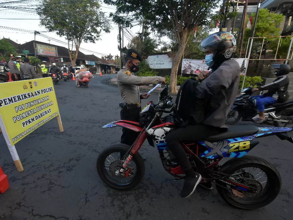 Anggota Polisi memeriksa surat keterangan kerja milik warga saat penyekatan Pemberlakuan Pembatasan Kegiatan Masyarakat (PPKM) Darurat di Pos Jalan Trengguli Penatih, Denpasar, Bali, Minggu (11/7/2021).  (photo/ANTARA FOTO/Nyoman Hendra Wibowo)