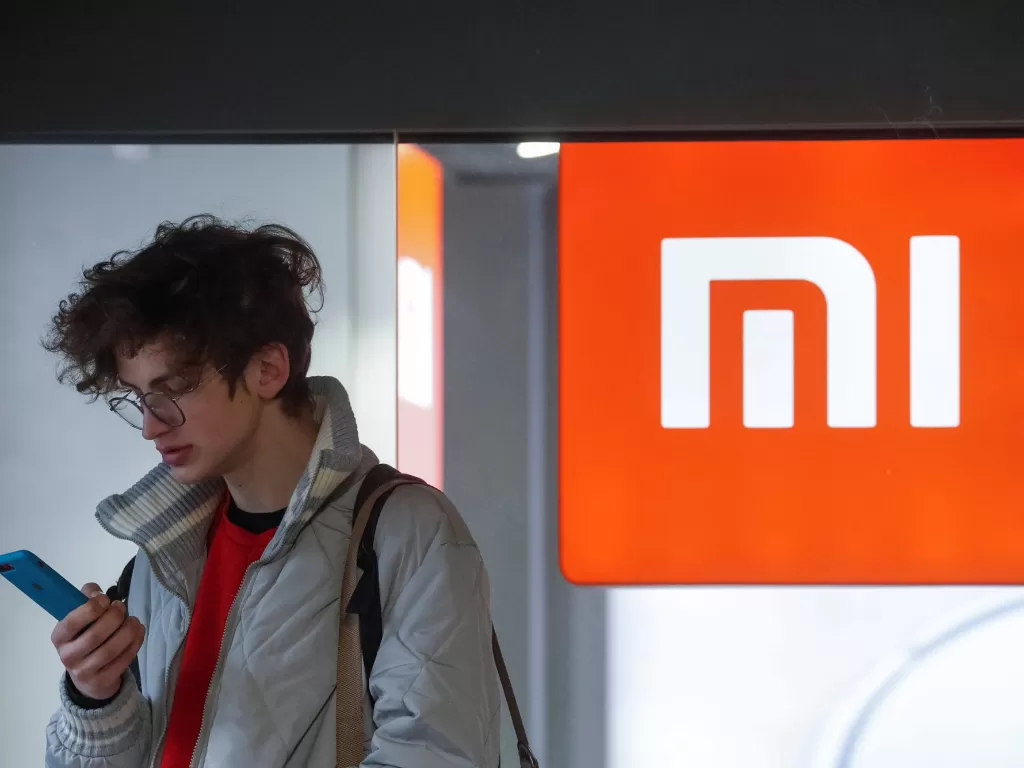 Seorang pria sedang berdiri di depan logo Xiaomi (photo/REUTERS/Valentyn Ogirenko)