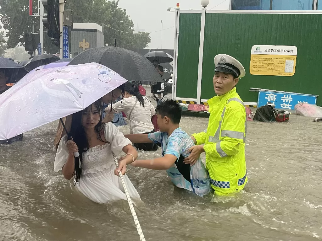 Seorang petugas polisi lalu lintas memandu warga untuk menyeberang jalan yang banjir dengan tali saat hujan deras di Zhengzhou, provinsi Henan, China 20 Juli 2021. (photo/China Daily via REUTERS)