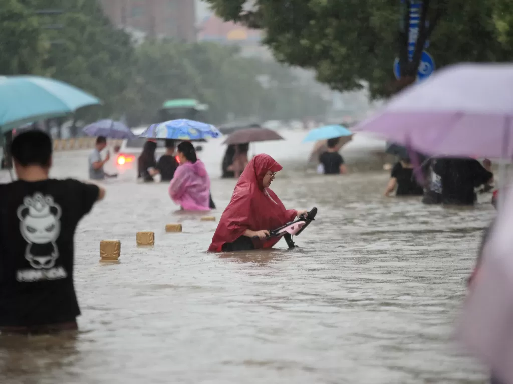 Warga mengarungi banjir di jalan yang banjir di tengah hujan deras di Zhengzhou, provinsi Henan, China 20 Juli 2021. (Photo/China Daily via REUTERS)