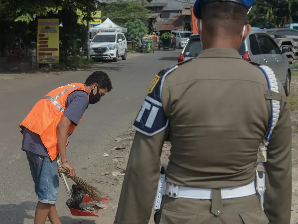  Petugas Satpol PP Jakarta Timur memberi sangsi kerja sosial pada warga yang melanggar protokol kesehatan saat operasi penertiban prokes dalam Pemberlakuan Pembatasan Kegiatan Masyarakat (PPKM) skala mikro di kawasan BKT, Duren Sawit, Jakarta Timur. (ANTA