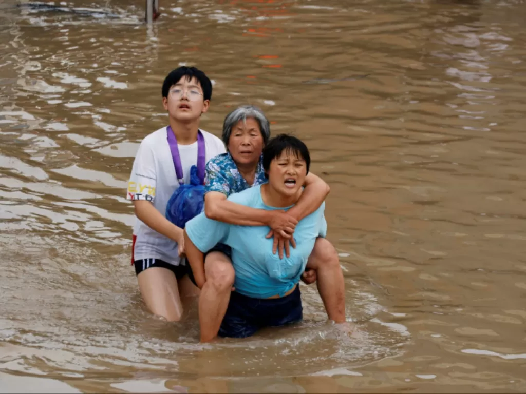 Seorang perempuan menggendong perempuan lanjut usia saat mereka berjalan melalui banjir menyusul hujan lebat di Zhengzhou, provinsi Henan, China, Jumat (23/7/2021). (REUTERS/ALY SONG) 