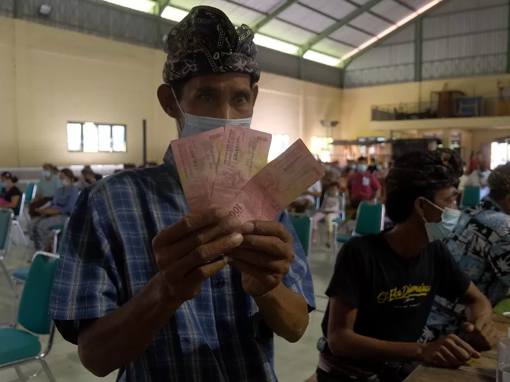 Warga menunjukkan tiga lembar uang Rp100 ribu dalam kegiatan Bantuan Langsung Tunai (BLT) (ANTARA FOTO/Nyoman Hendra Wibowo/hp.)