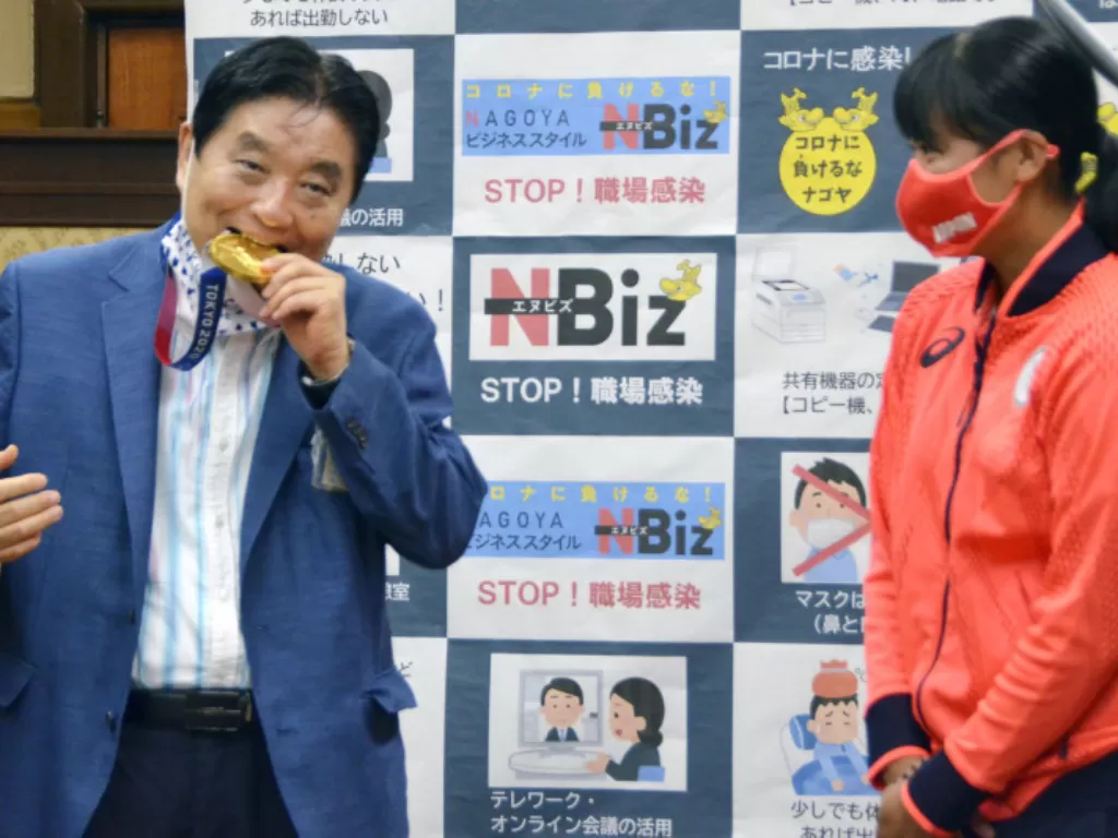 Wali Kota Nagoya Takashi Kawamura menggigit medali emas Olimpiade Tokyo milik atlet sofbol Jepang Miu Goto dalam sebuah acara di Nagoya, Jepang tengah, Rabu (4/8/2021). (REUTERS/KYODO)