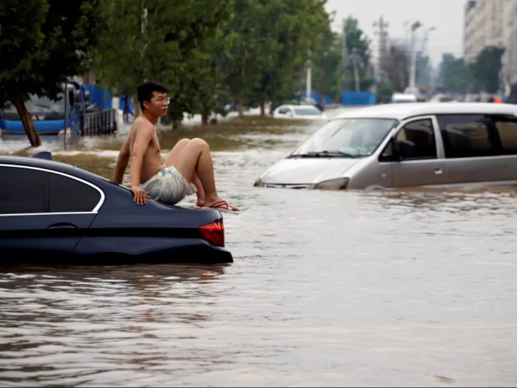 Seorang warga terjebat di tengah banjir yang melanda beberapa daerah di China (REUTERS/Aly Song)