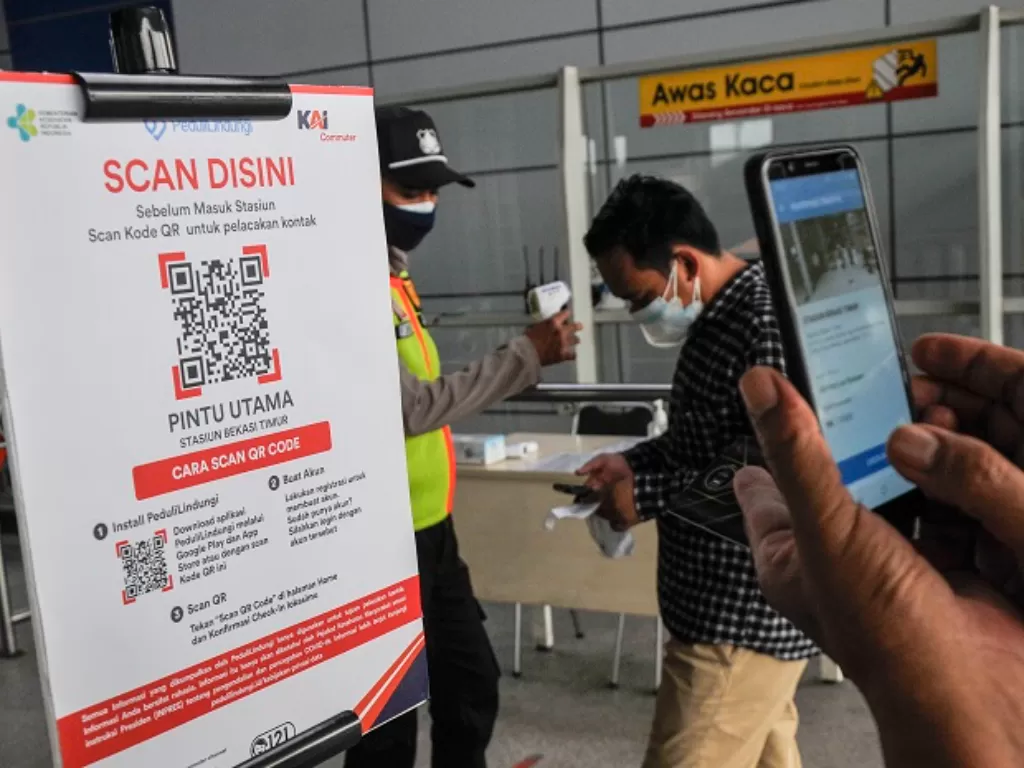 Petugas (kiri) mensosialisasikan kepada calon penumpang KRL (Kereta Rel Listrik) untuk memindai kode batang (QR Code) sebelum memasuki peron Stasiun Bekasi Timur. (ANTARA FOTO/ Fakhri Hermansyah)