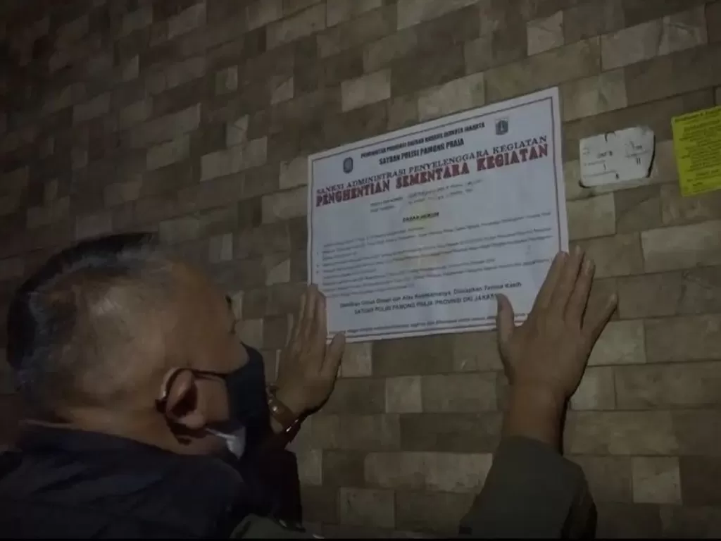 Petugas memasang segel bertuliskan 'Penghentian Sementara Kegiatan' pada dinding tempat hiburan malam yang melanggar ketentuan usaha selama PPKM Level 3 di Penjaringan, Jakarta Utara, Kamis (9/9/2021). (photo/Instagram/@satpolpp.dki)