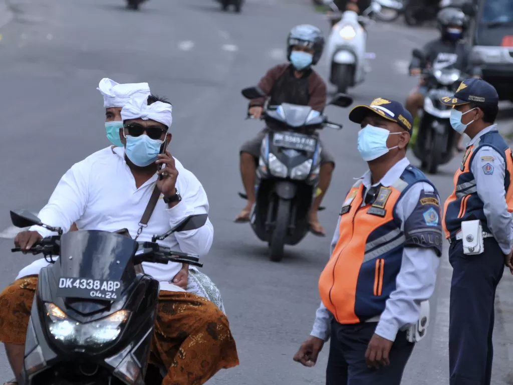 Pengendara yang mengenakan masker melintas di dekat petugas yang melakukan sidak protokol kesehatan di Denpasar, Bali, Jumat (13/8/2021). (ANTARA/Fikri Yusuf)