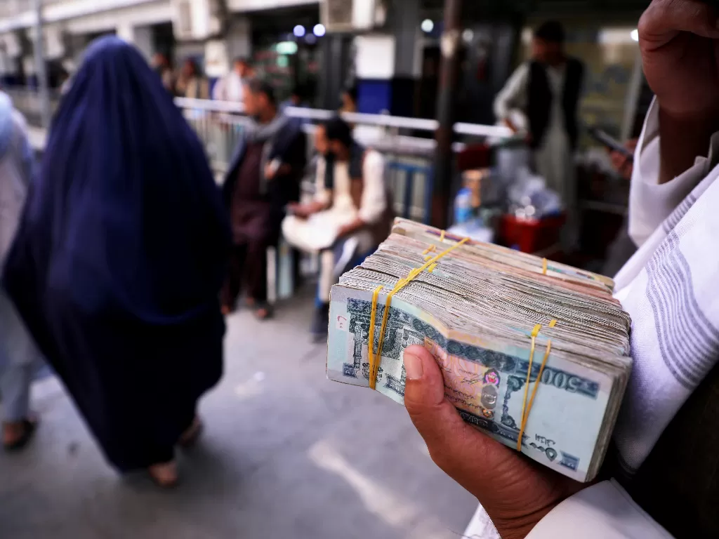 Seorang pria memegang seikat uang kertas Afghanistan di pasar pertukaran uang. (REUTERS/Stringer)