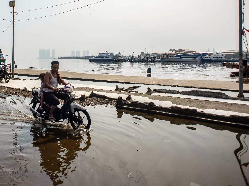 Warga mengendarai motor melintasi genangan air laut di kawasan Pelabuhan Kali Adem, Muara Angke, Jakarta (ANTARA FOTO/Aprillio Akbar/rwa.)