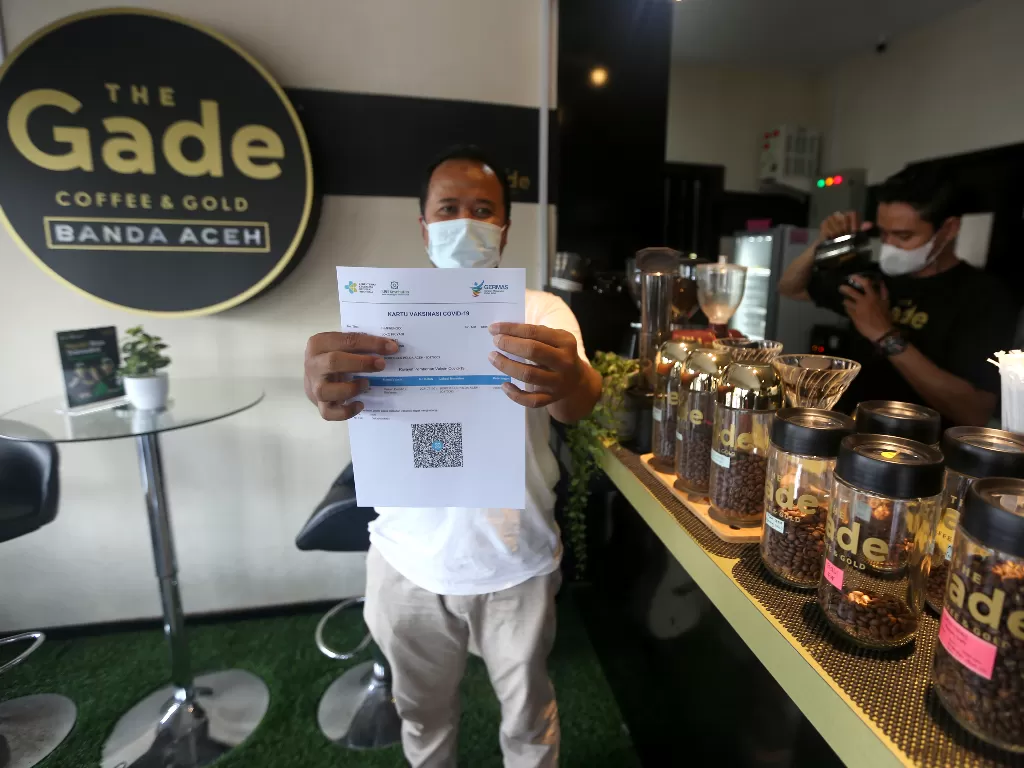 Pengunjung salah satu warung kopi (warkop) memperlihatkan sertifikat vaksin COVID-19 seusai mendapatkan suntikan yang digelar Polda Aceh di Banda Aceh, Aceh, Minggu (10/10/2021) (ANTARA FOTO / Irwansyah Putra).