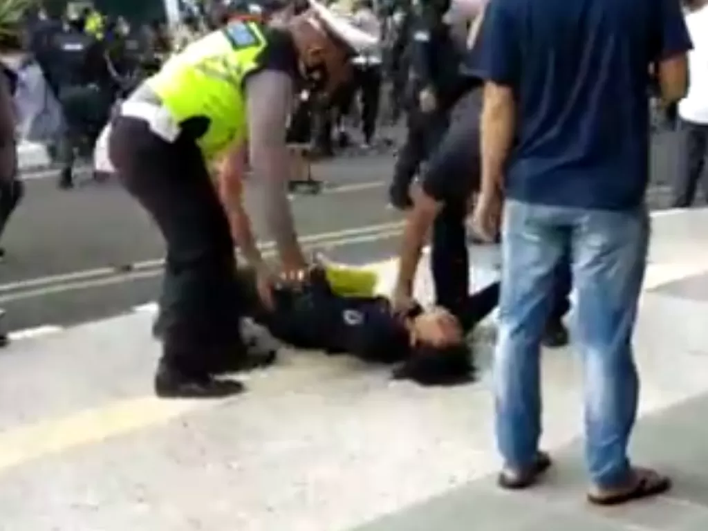 Polisi mencoba membangunkan mahasiswa yang pingsan usai dibanting polisi berseragam huru-hara. (Tangkapan layar Twitter)