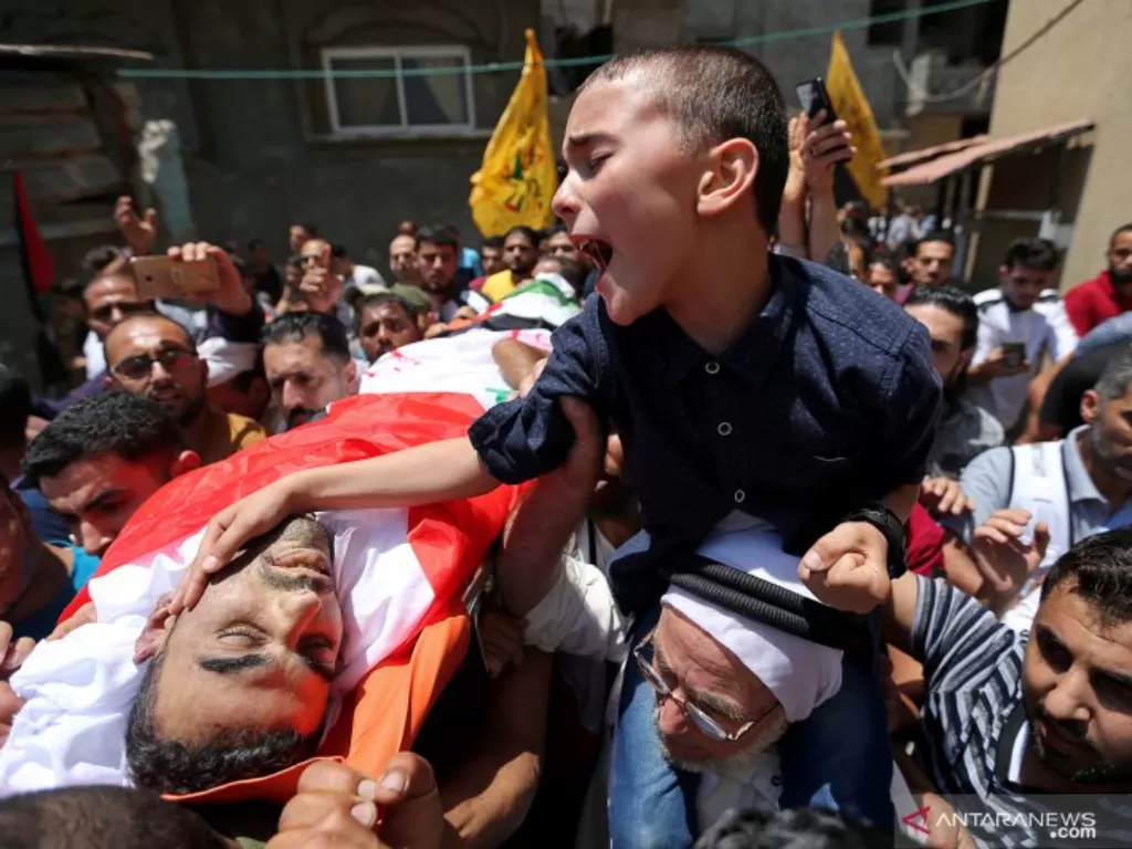 Seorang anak lelaki petugas medis Palestina Mohamed Al-Judaily menangis melihat jenazah ayahnya dalam pemakaman di pusat Jalur Gaza. (REUTERS/Ibraheem Abu Mustafa)