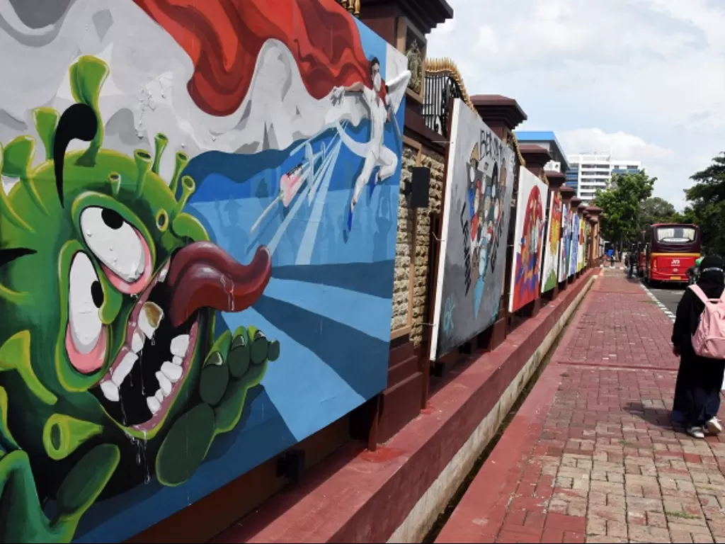 Warga melintas di dekat mural bertema pencegahan Covid-19 di Jakarta. (ANTARA FOTO/Indrianto Eko Suwarso)