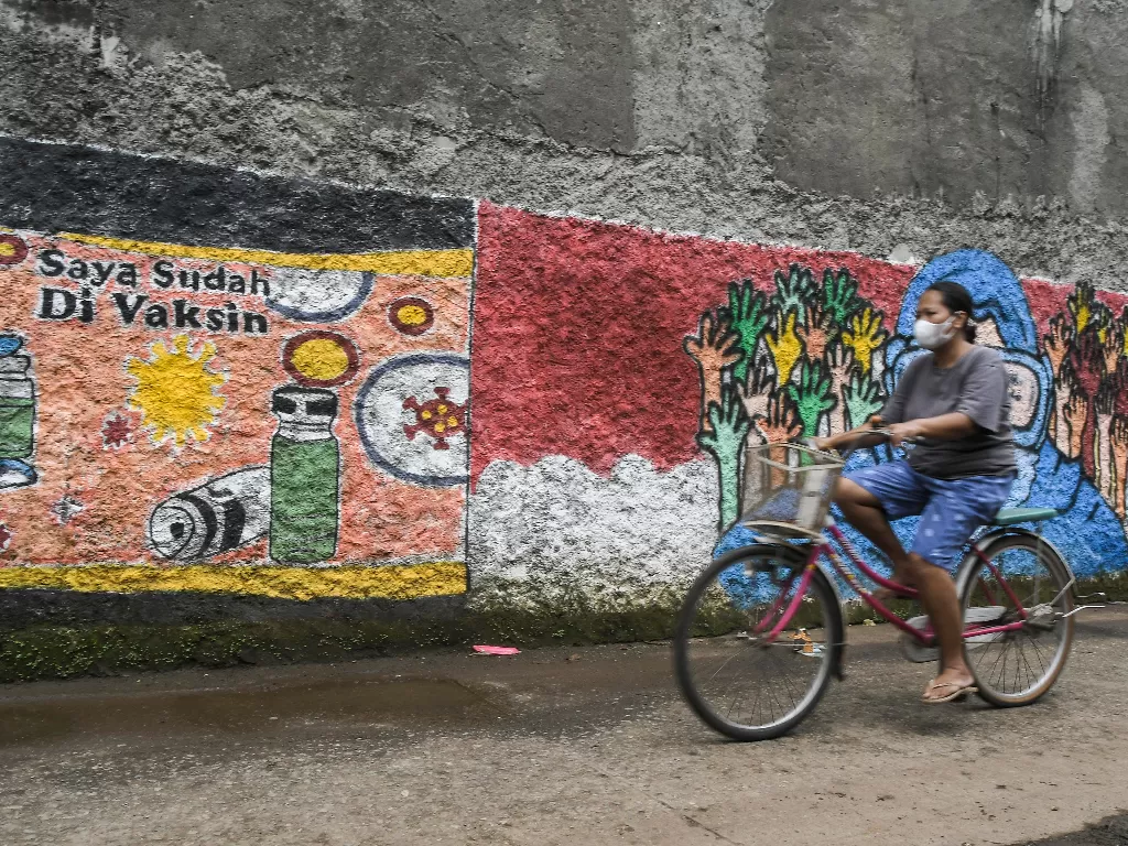 Pengendara sepeda melintasi mural bertemakan sosialisasi untuk vaksinasi Covid-19 di Bekasi, Jawa Barat, Senin (15/11/2021). (ANTARA FOTO/Fakhri Hermansyah/hp)