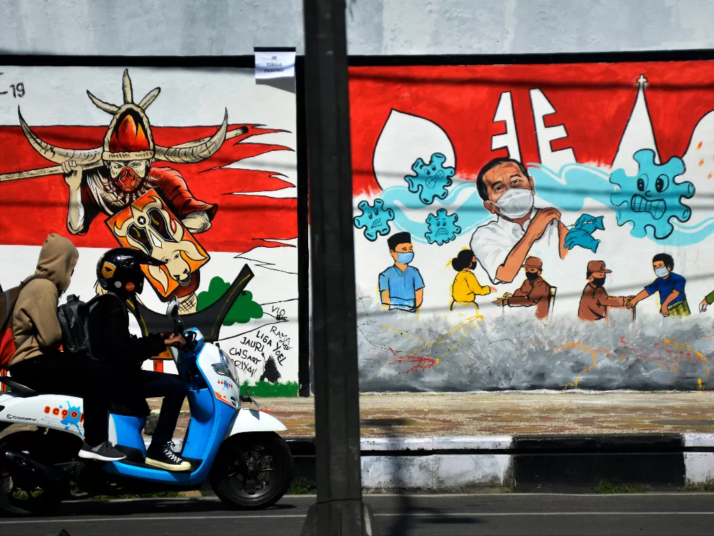 Pengendara melintas di depan mural bertema Covid-19 di kawasan Jalan Nusantara, Makassar, Sulawesi Selatan, Senin (1/11/2021). (ANTARA FOTO/Abriawan Abhe/wsj)