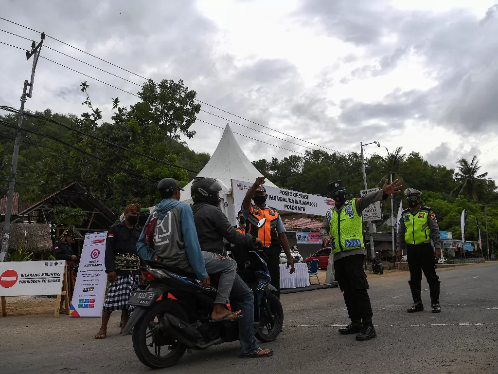 Anggota Polisi mengarahkan pengendara motor untuk mencari jalan lain di pos penyekatan kendaraan, Kuta Mandalika, Lombok Tengah, Nusa Tenggara Barat. (Foto: ANTARA/Sigid Kurniawan)