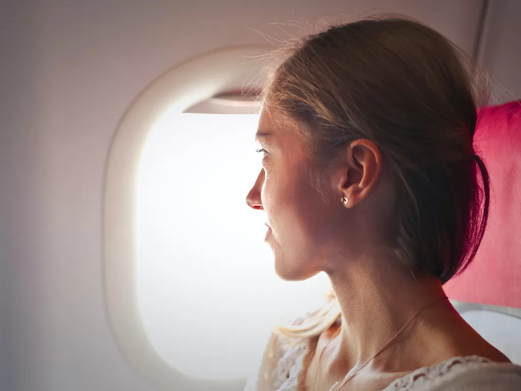 Seorang wanita melihat kaca jendela pesawat. (photo/Ilustrasi/Pexels/Adrienn)