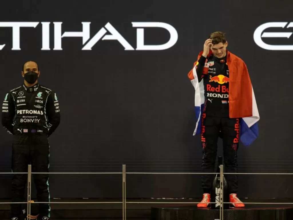 Pebalap Red Bull Max Verstappen merayakan kemenangan sekaligus menjadi juara dunia dengan bendera Belanda di podium, sementara pebalap Mercedes Lewis Hamilton tampak sedih setelah finis di urutan kedua Grand Prix Abu Dhabi di Sirkuit Yas Marina, Abu Dhabi
