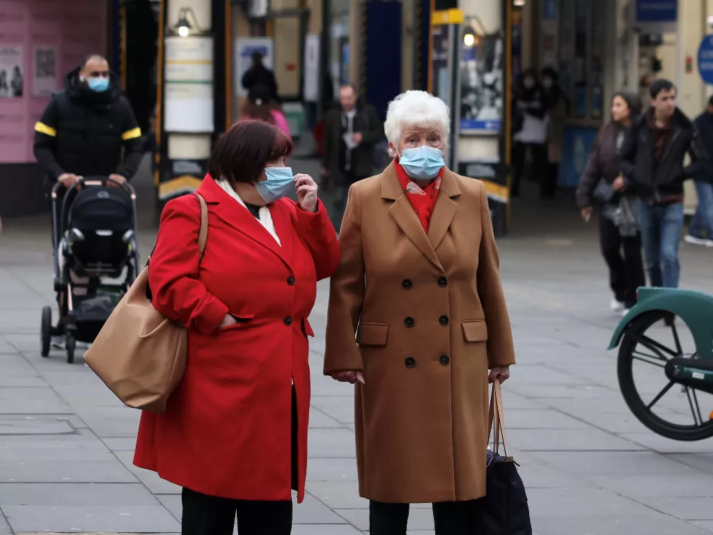 Wanita yang memakai masker menunggu untuk menyeberang jalan di tengah wabah penyakit virus corona (COVID-19) di London, Inggris. (REUTERS/KEVIN COOMBS)